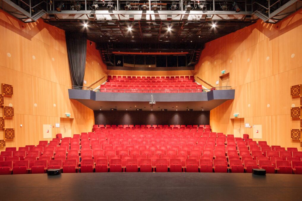 Theaterzaal met rode stoelen en een balkon vanaf het podium.